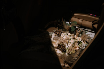 A bridal bouquet with roses and various foliage is illuminated by a beam of light inside a car,...