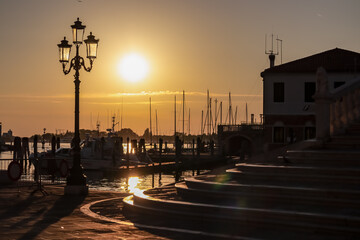 First rays of sunrise illuminate steps of bridge Ponte di Vigo stretching across the enchanting Canal Vena in Chioggia, Venetian Lagoon, Veneto, Italy. Exquisite display of Venetian architecture
