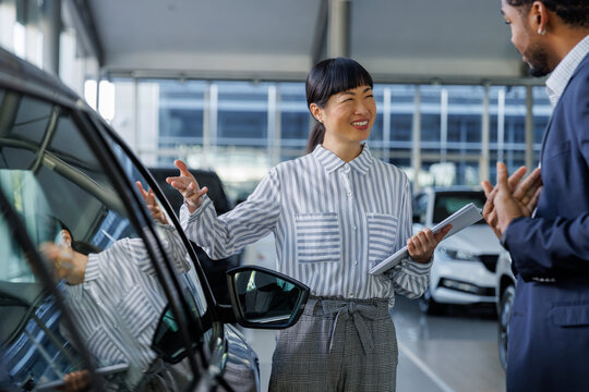 Asian sales manager showing new car to customer
