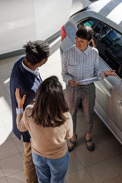 Sales manager showing new car to couple at dealership