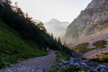 Hiking trail to ridge Begunjscica at sunrise in untamed Karawanks, border Austria Slovenia, Europe. Hiking on Loibl Pass, Slovenian Alps. Steep mountains blazed crimson with first rays of morning sun