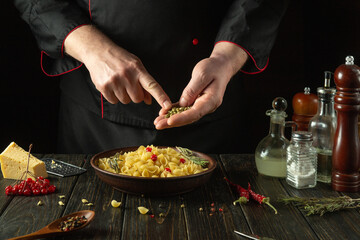 Adding aromatic spices to a bowl of pasta. The cook at the kitchen table prepares a delicious...