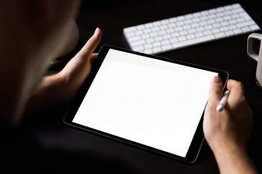 Male hands holding an empty tablet and pen in an artist workspace.