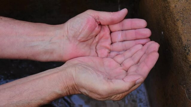 Recoger agua con las manos. El hombre junta sus manos para aprovechar las gotas del grifo por la escases de la sequ&iacute;a del cambio clim&aacute;tico para beber. 