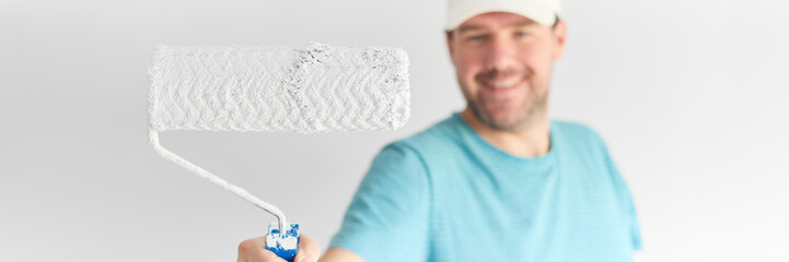 Young man holding a roller in front of himd - small depth of field.  The idea of painting the walls white.