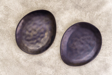 Pair of empty black irregularly shaped plates on beige concrete background. Top view, with copy space - 777700542