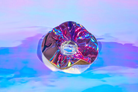 Old damaged CD disc lying over holographic background