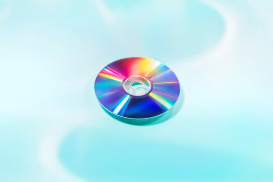 Compact disc refracting rainbow light on blue background