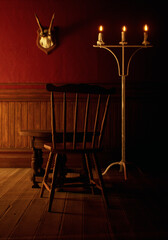 Vintage rustic interior with wooden floor, wooden table, wooden chair, paneling, candlestick and deer skull on the wall.
