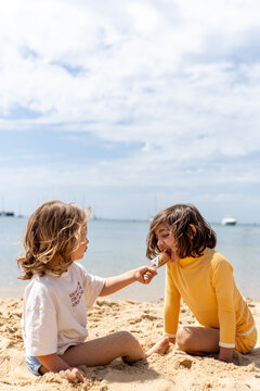 Two kids playing at the beach and eating ice cream