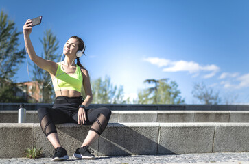 happy woman taking selfie in a park with sportswear after running and headphones