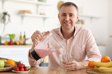 Mature man pouring fruit smoothie into glass in kitchen