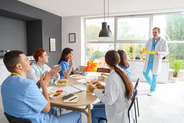 Team of doctors having lunch at table in hospital kitchen - obrazy, fototapety, plakaty