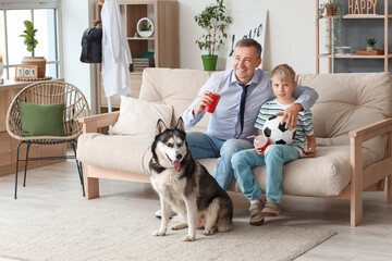 Mature doctor with his little son and dog watching football game at home - obrazy, fototapety, plakaty