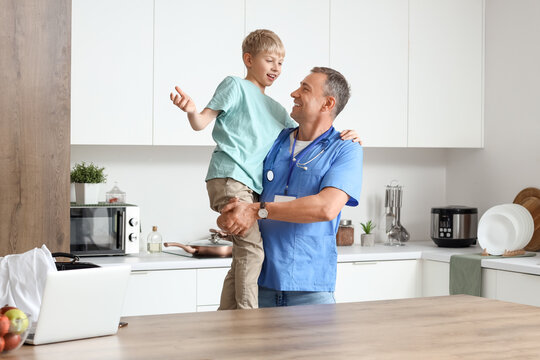 Mature doctor holding his little son in kitchen