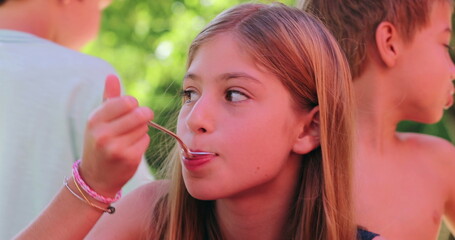 Candid children outside together, little girl eating dessert sweek snack with spoon, dulce de leche