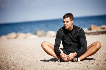 Man, exercise and sports at ocean for stretching with fitness motivation, sand and blue sky. Male person, training and nature by beach with workout for wellness, strong body and health activity