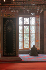 A muslim man sitting and praying in front of the window in the mosque and sunlight during the...