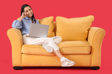 Fototapeta na wymiar Beautiful young happy woman with laptop resting on sofa against red background