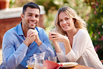 Portrait, happy and couple eating breakfast in garden outside at table in morning. Married, man and woman on romantic getaway at house sitting on patio talking, coffee and care for relationship