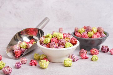 Bowls and metal scoop with sweet colorful popcorn on white background