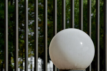 biala kula na tle metalowego ogrodzenia z prętów, lampa kula na tle ogrodzenia, abstrakcja, ball...