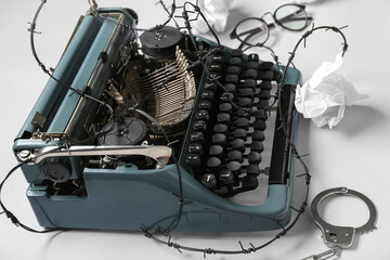 Vintage typewriter with barbed wire, handcuffs and crumpled paper on white background. Printing ban...