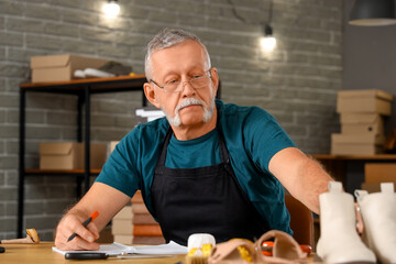 Mature shoemaker writing at table in workshop