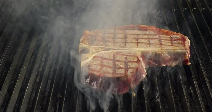 Close-up T-bone meat steak on barbecue charcoal grill. Grilling BBQ meat. Smoke rising over juicy beef steak