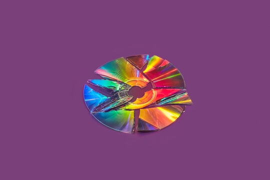 Compact CD disc broken into small pieces over dark violet background