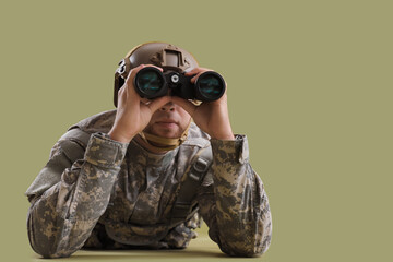 Lying male soldier in uniform looking through binoculars on green background