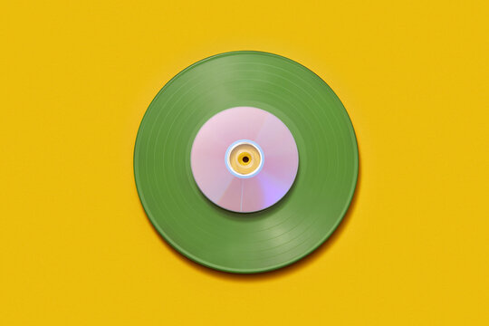 CD disc placed on top of green vinyl record over yellow background