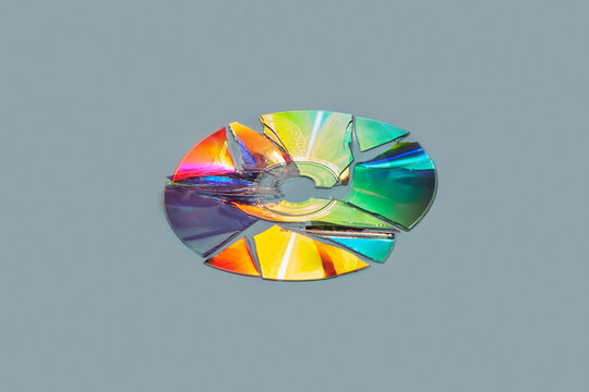 Broken compact CD disk refracting rainbow light on surface