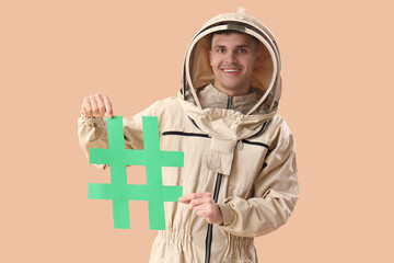Male beekeeper in protective clothing with hashtag sign on color background - Powered by Adobe