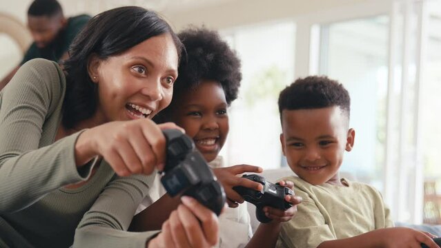Mother and children playing handheld computer game at home with multi generation family in background - shot in slow motion