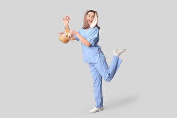 Happy female dentist in bunny ears with Easter basket and jaw model on grey background