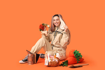 Happy female beekeeper in bunny ears with Easter basket, toy carrots and tools sitting on orange...