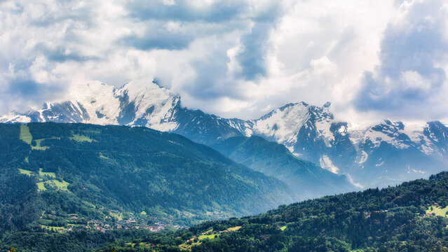 Mont-Blanc massif, covered by stormy clouds, as viewed from the A40 highway, in France. The town of Saint-Gervais-les-Bains is visible in the valley ahead.