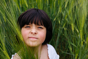 close up portrait of smiling girl with dark hair sitting in a field of wheat - obrazy, fototapety, plakaty