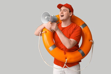 Male lifeguard with ring buoy and megaphone on grey background