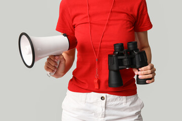 Female lifeguard with megaphone and binoculars on grey background