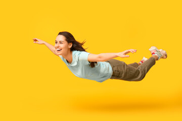 Joyful young woman flying on yellow background