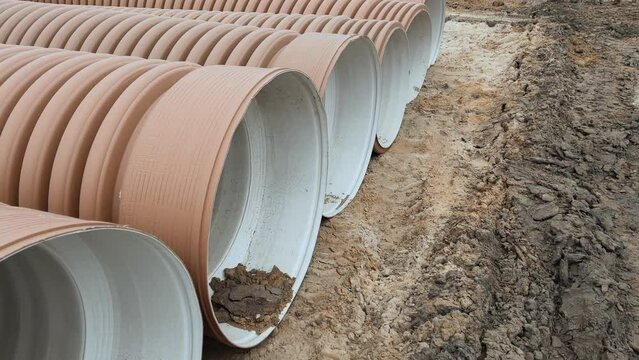 Corrugated Double-Walled Polypropylene Pipes Lined Up at a Construction Site During Daytime. Several large red corrugated plastic pipes on a dirt ground, likely for drainage or utilities.