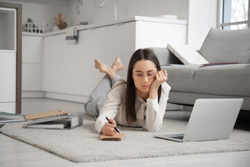 Tired young businesswoman lying on floor with laptop and notebook at home - obrazy, fototapety, plakaty