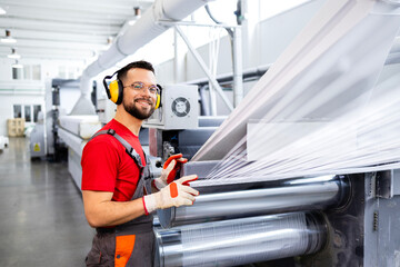 Production line worker standing by machine and controlling plastic bag manufacture. - obrazy, fototapety, plakaty