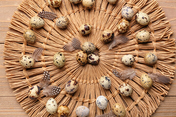 Wicker mat with fresh quail eggs and feathers on wooden background