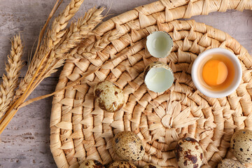 Wicker mat with fresh quail eggs and wheat on grey wooden background