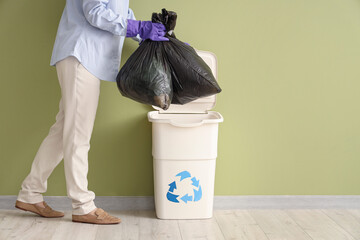 Woman with garbage bags and trash bin near green wall