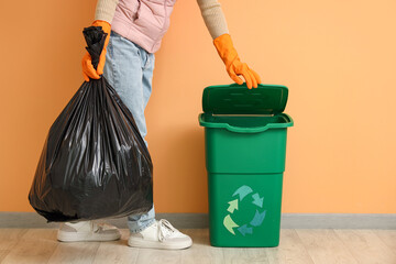 Woman taking garbage bag from trash bin near orange wall
