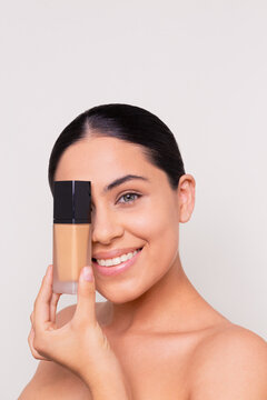 Young woman holds a makeup foundation in front of her face